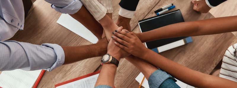 Multicultural team. Top view of business people holding hands together while sitting in the office. Teamwork. Success